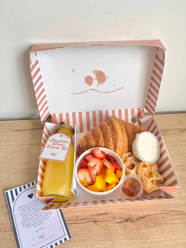 Snack en caja de rayas con croissant, jugo de naranja y fruta